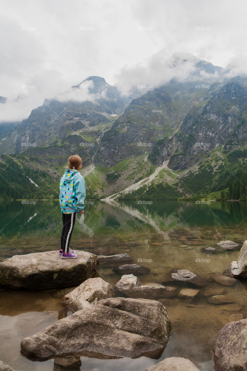 Little girl admiring polish Tatra Mountains from banks of Morskie Oko. Translation: Eye of Sea Lake. Poland. Europe.