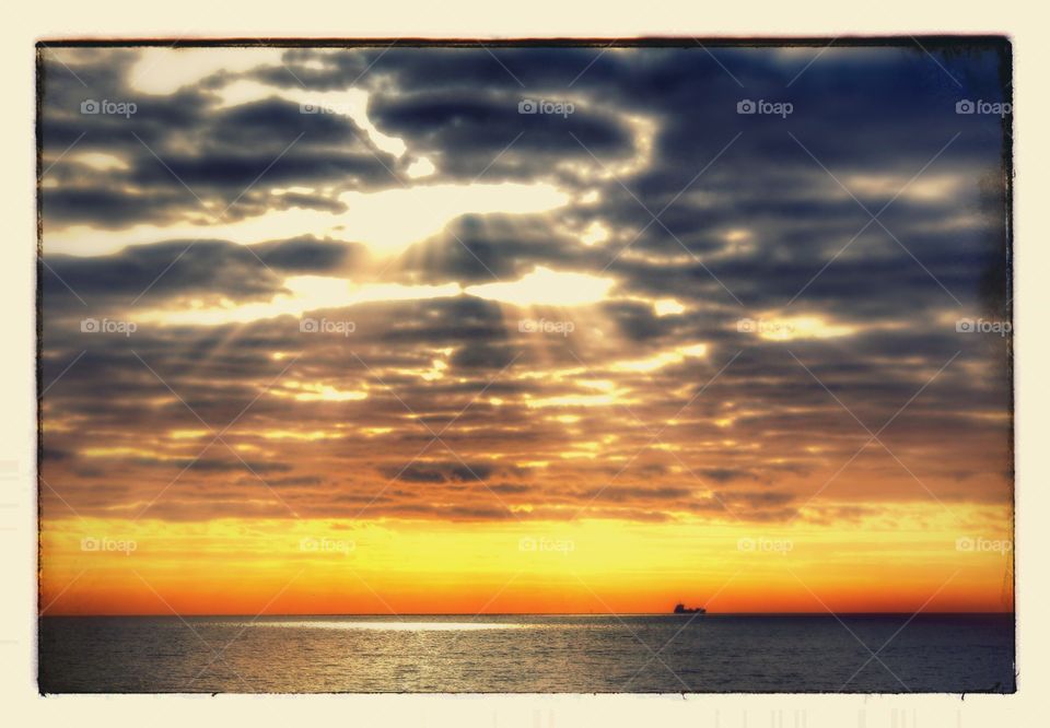 Sun beams peeping through the dark cloud making a spotlight effect over the water. 