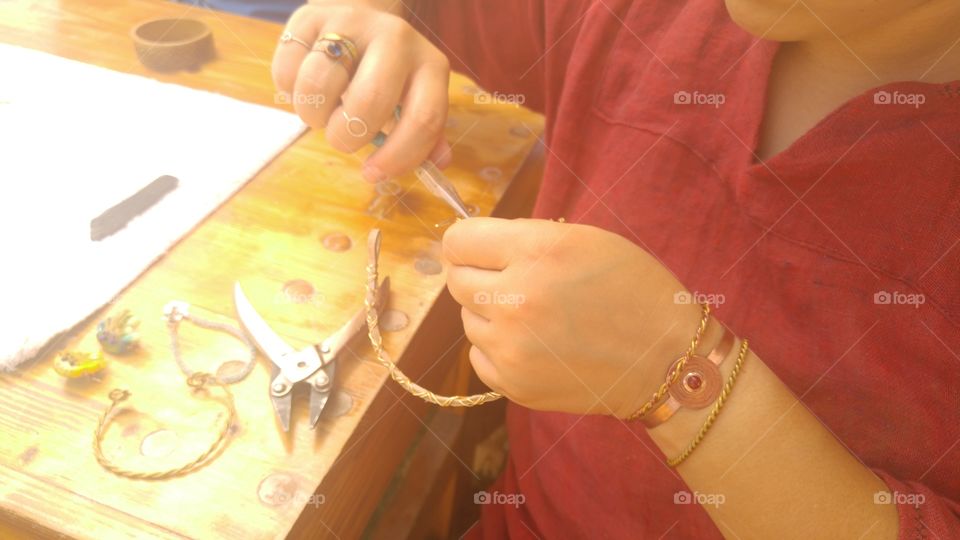 a woman demonstrates how she makes braided metal jewelry