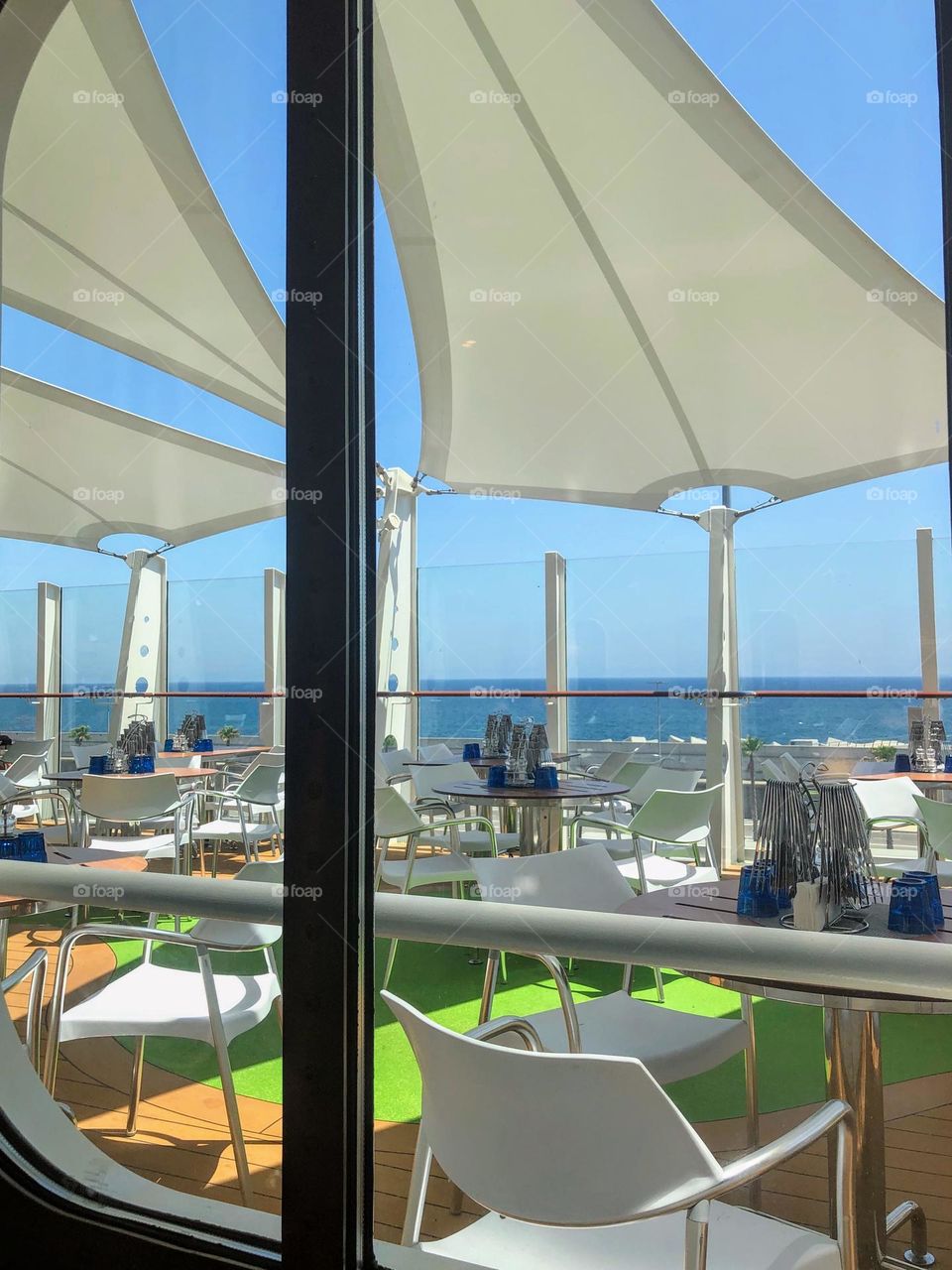 View from the luxury cruise ship to the open deck restaurant with tables, chairs and glass fence under the sun protection tents 