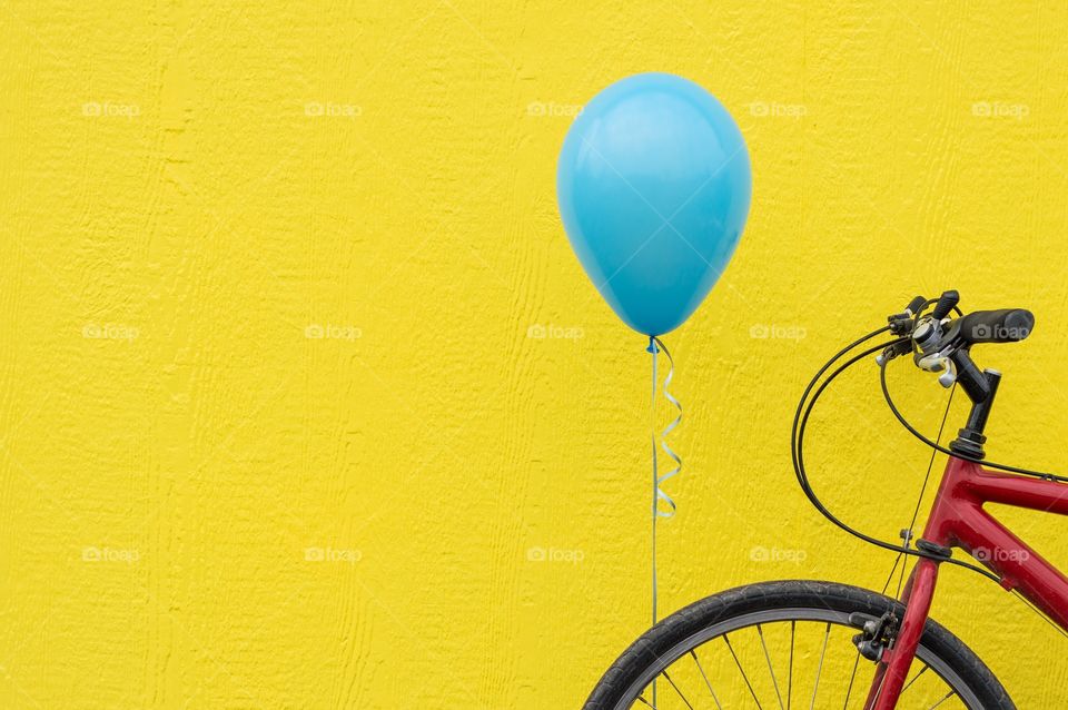 Balloon, bicycle, and wall. Red bicycle with a blue balloon against a bright yellow wall.