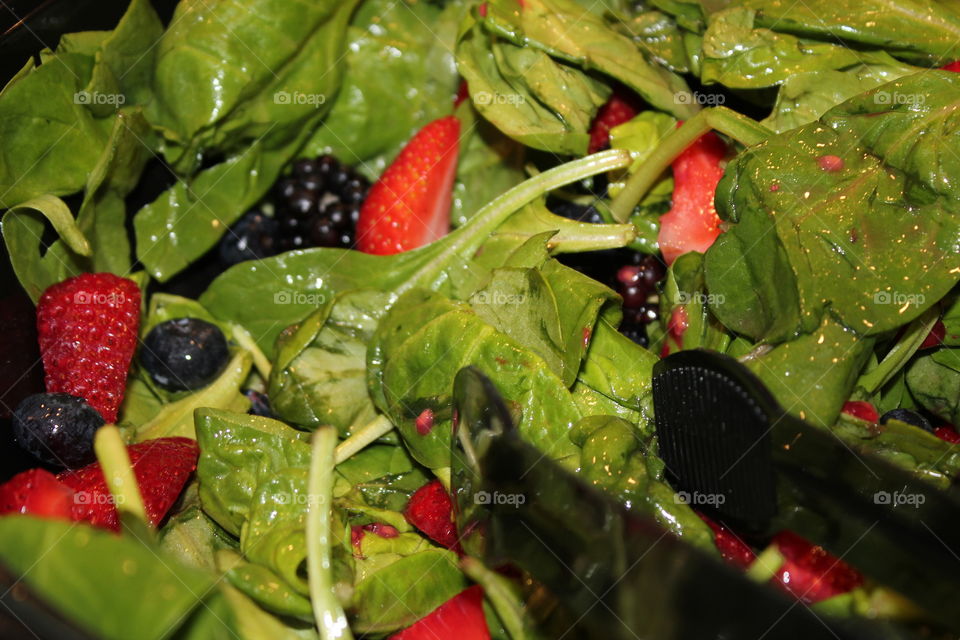 Spinach and berry salad with tongs