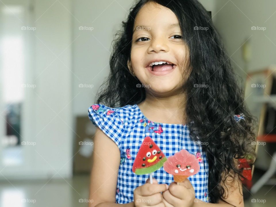 3 years old girl having two candy’s in her hand and having smiley face.