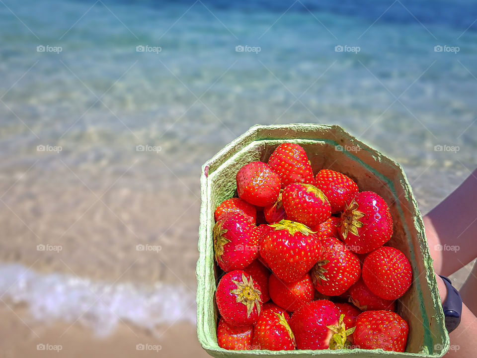Fresh strawberries in a cardboard box on a background of the sea. Summertime and concept of world without plastic.