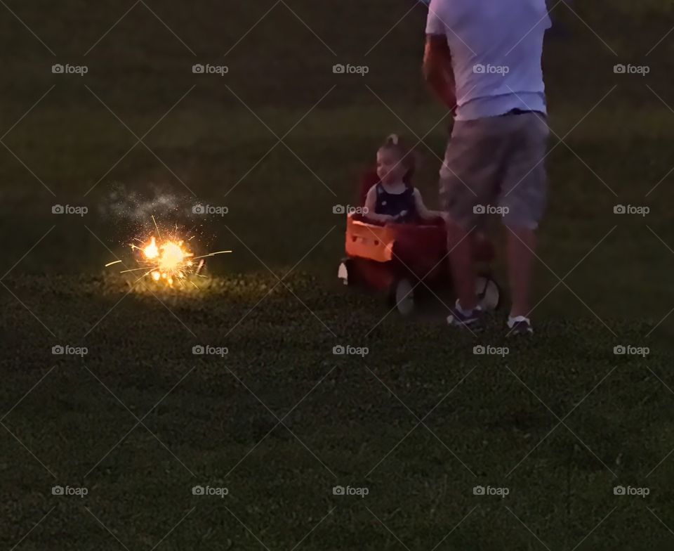 Tiny girl and her Father enjoying the  dazzling glow from sparklers. 