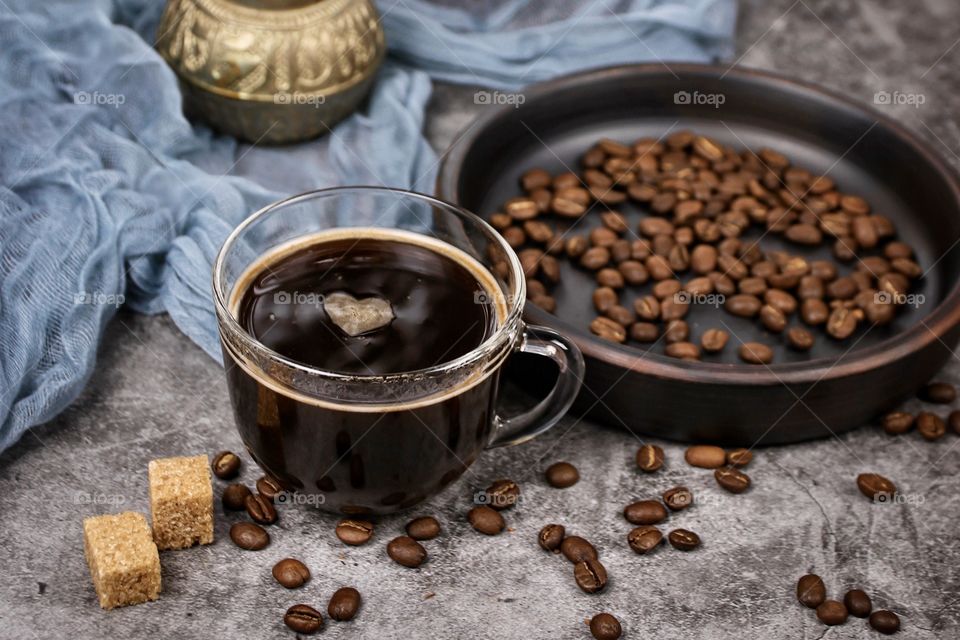 transparent cup with black coffee and sprinkled coffee beans