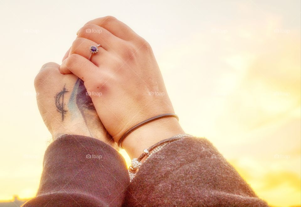 Engaged couple holding hand up against the sky showing engagement ring
