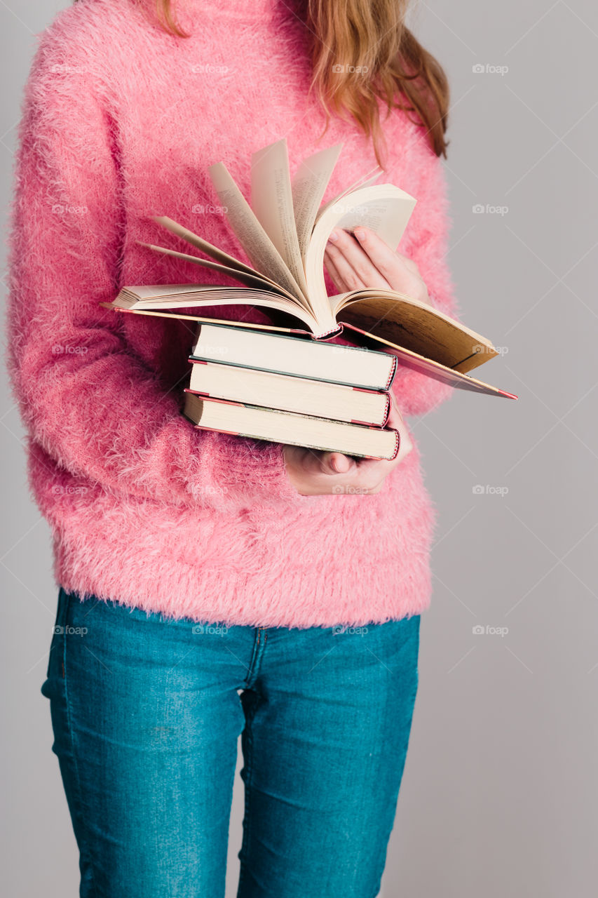 Young girl holding a few books. Teenager girl wearing pink sweater and blue jeans. Vertical photo