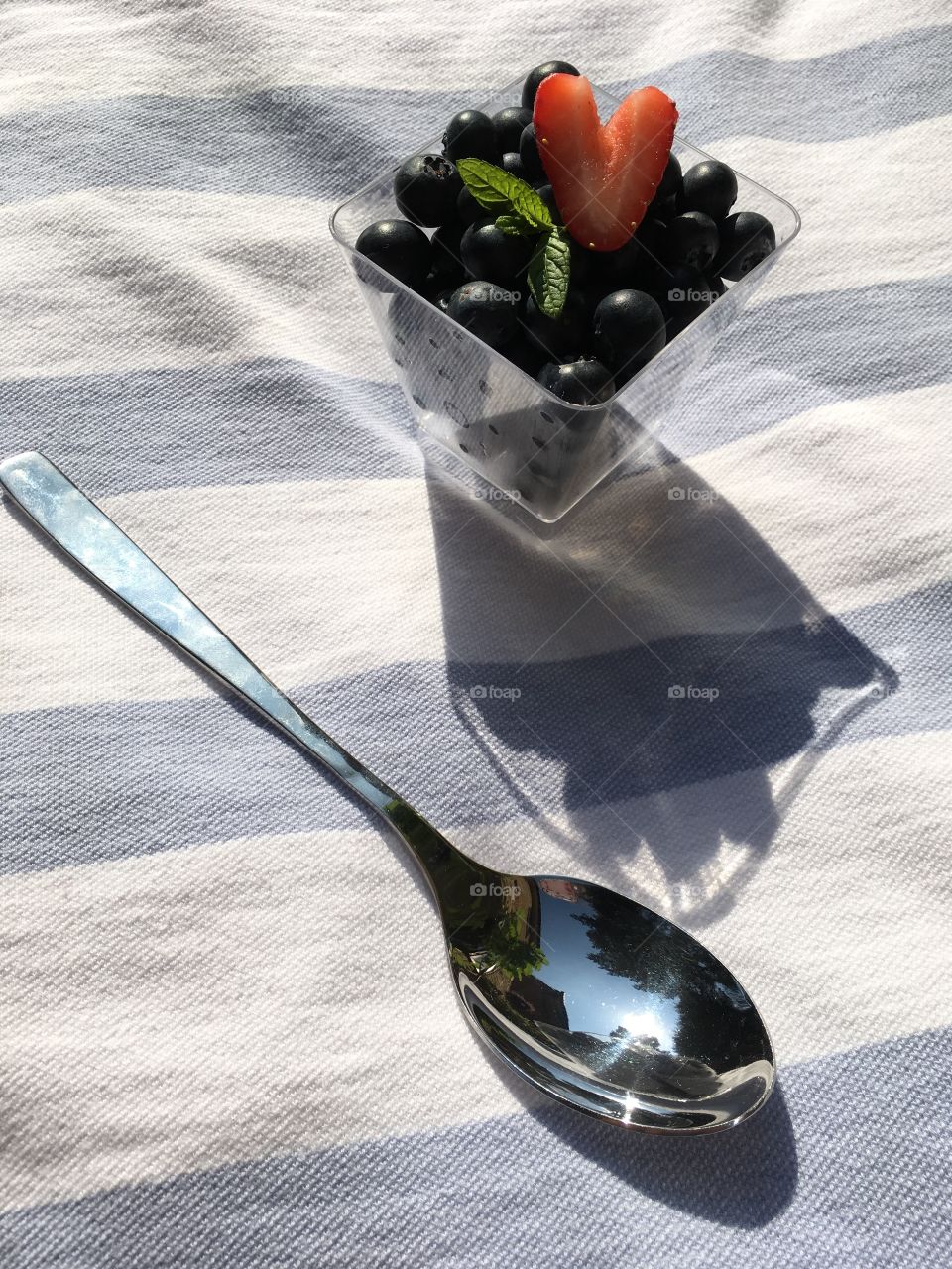 Dish of blueberries with a heart shaped strawberry and a sprig of mint and a spoon