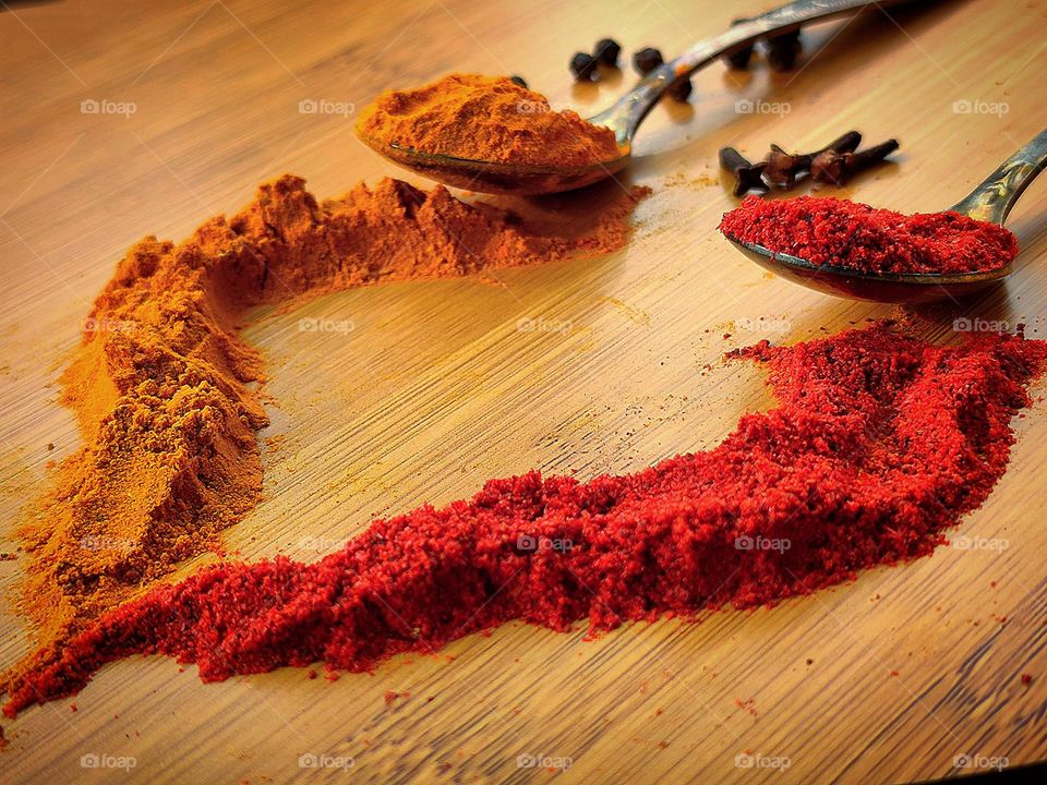 Autumn colors. There are two spoons on a wooden surface. Orange curry and red paprika. Spices are scattered in the form of a birch leaf