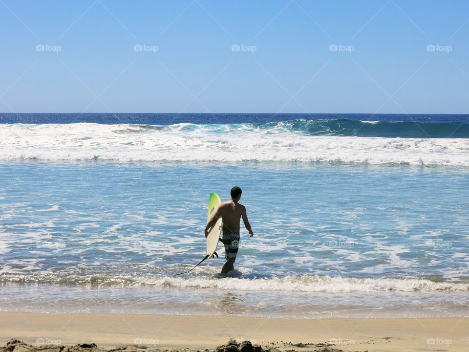 Man in a bathing suit walks into the Pacific Ocean to catch some waves in Encinitas, California. 