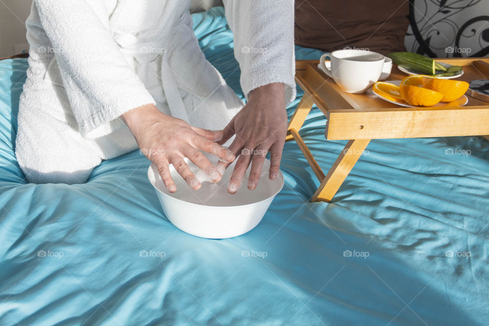 A man at home takes care of himself and does a manicure at home on a blue background and with orange.