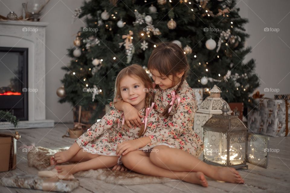 Little sisters near Christmas tree at home