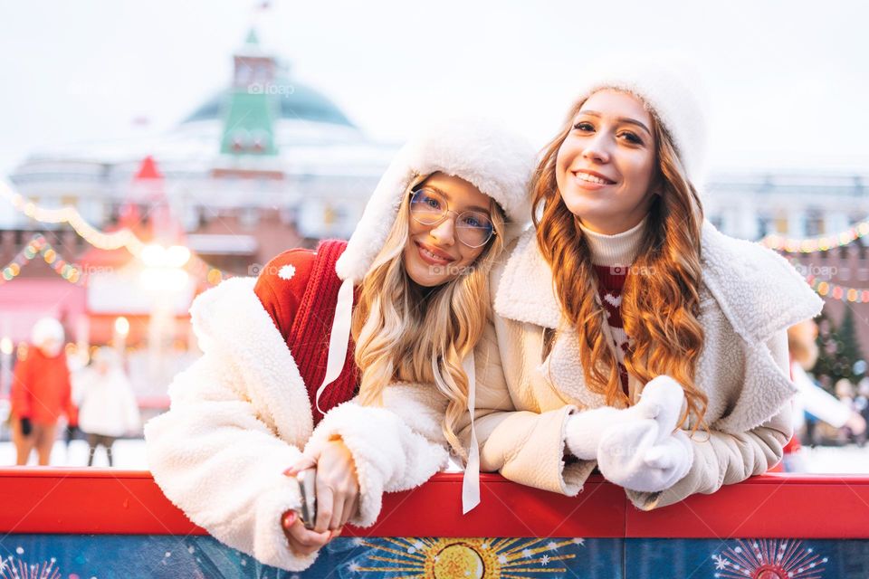 Young happy women friends with curly hair in red having fun in winter street decorated with lights