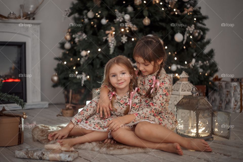 Little sisters near Christmas tree at home