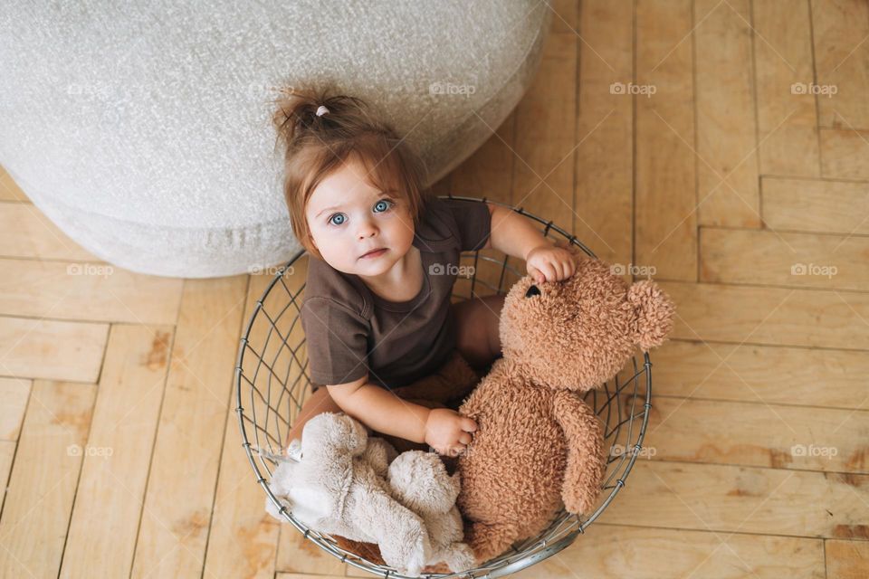 Portrait of cute baby girl sitting in basket with soft toys at home