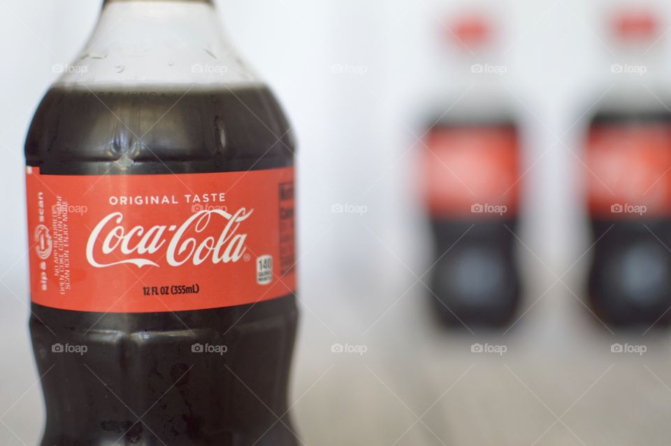 Two plastic bottles of Coca-Cola on a white rustic background