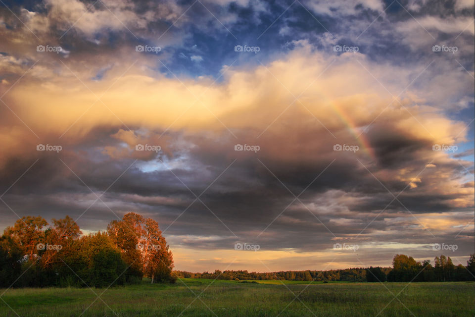 Summer landscape with rainbow at cloudy day