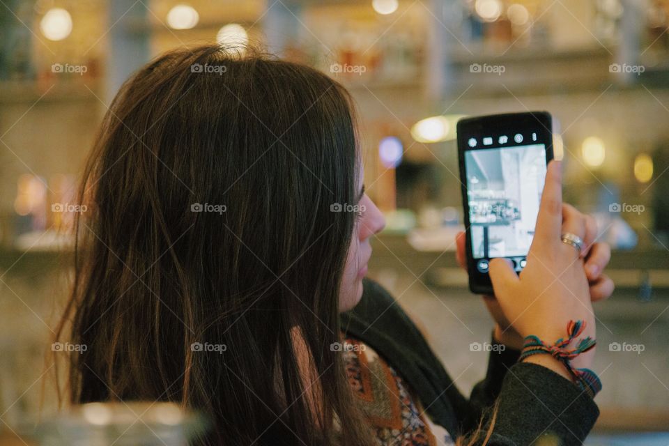 A young woman taking pictures of a cafe on her phone