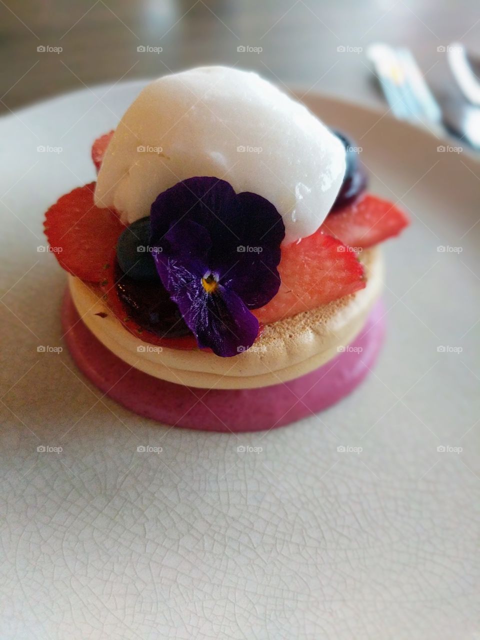 Purple flower on an dessert with red strawberries, brown biscuit and white cream