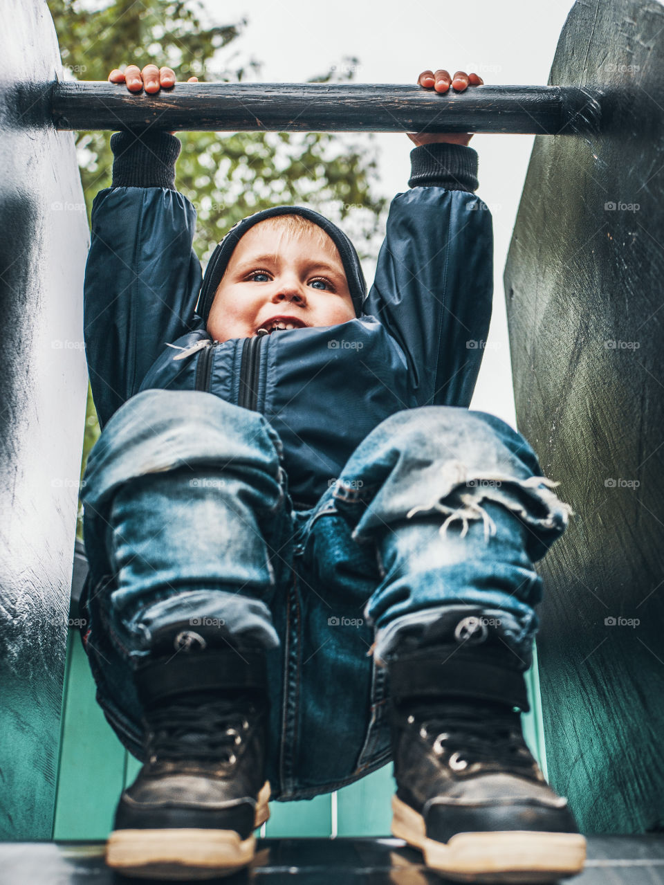 Boy playing on playground, about to go down a slide. Wearing a blue bomber jacket and jeans.