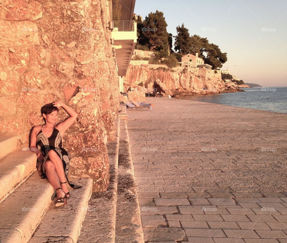 Smiling woman sitting on steps against wall near sea