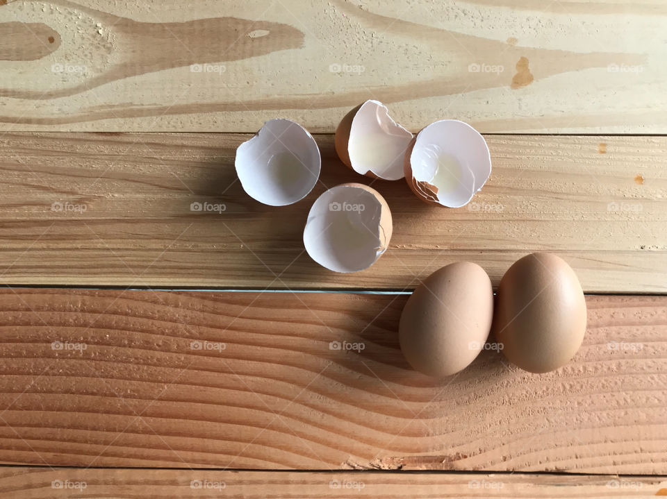 top view shot of two fresh organic chicken eggs with four pieces of eggshells on natural rubber wood board table with copy space on left side of frame