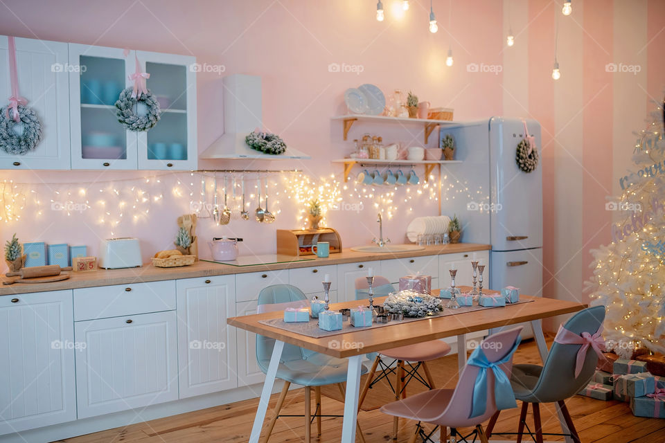 Festive winter cozy kitchen interior with garlands, decorations and gifts.  Christmas dinner at the decorated table.