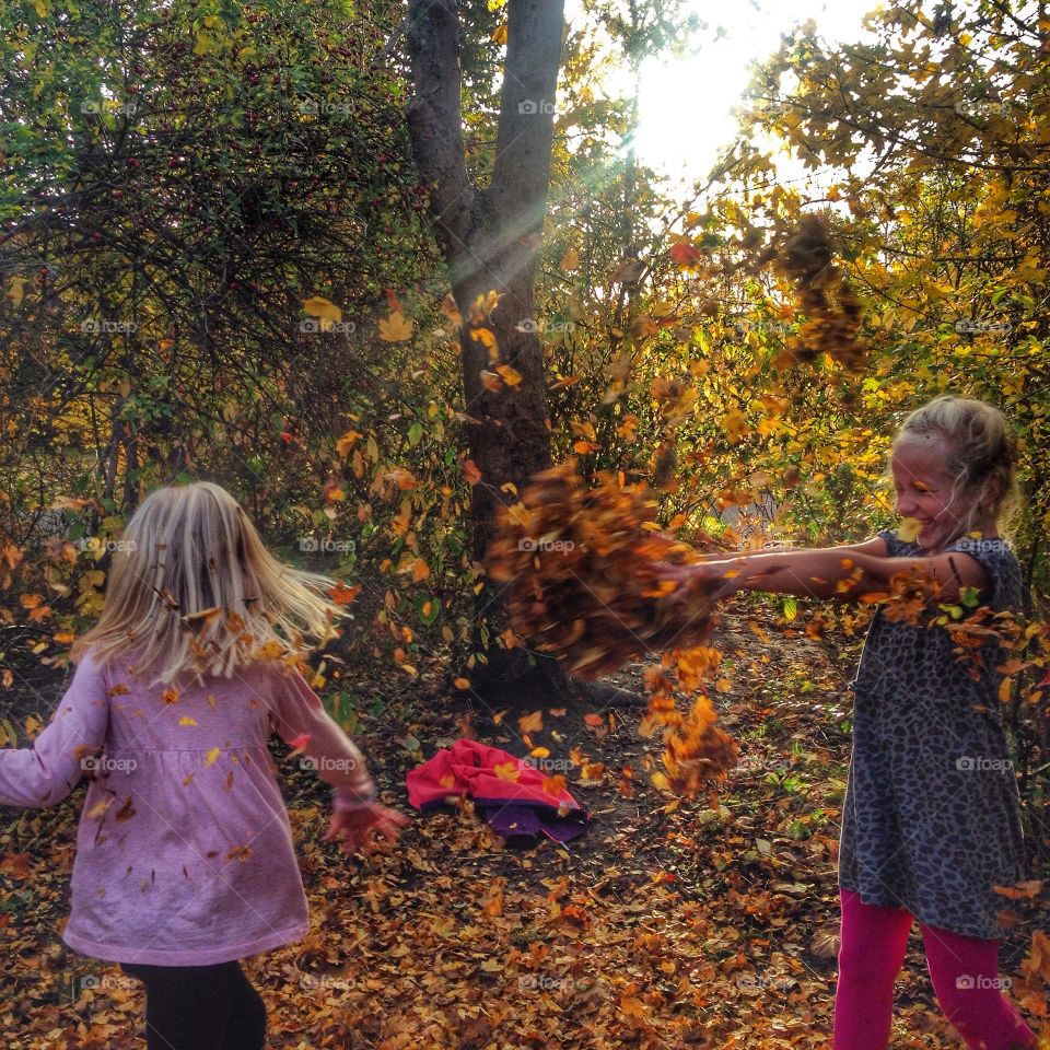 Happy sisters playing with leaves during autumn