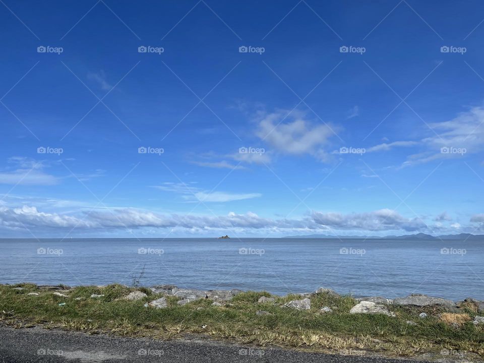 Beautiful blue ocean and fluffy clouds in line and clear blue sky as background 