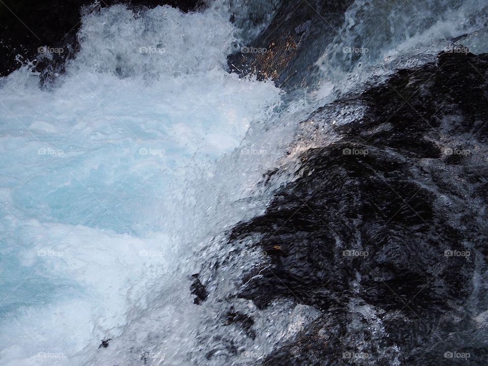 Rays of golden sunlight hit the rapid turquoise waters of the McKenzie River in the forests of Oregon as it rushes over rocks on a fall evening. 