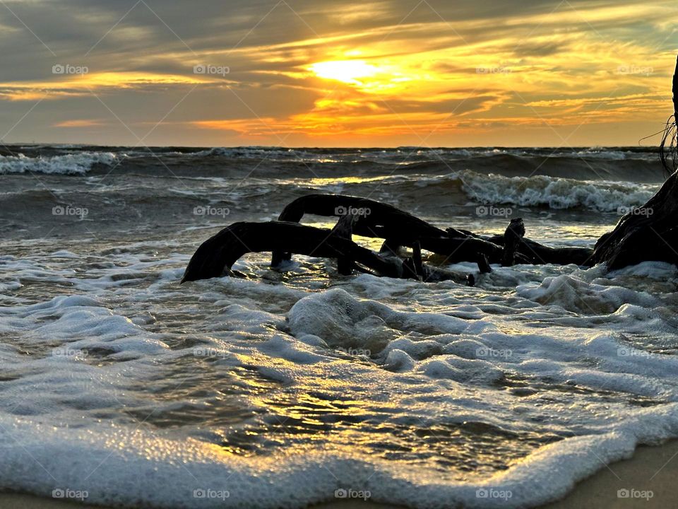 A breathtaking sunset as the waves, often towering and frothy, collide with the shore with great force, sending spray and foam into the air creating a stunning display of energy and motion