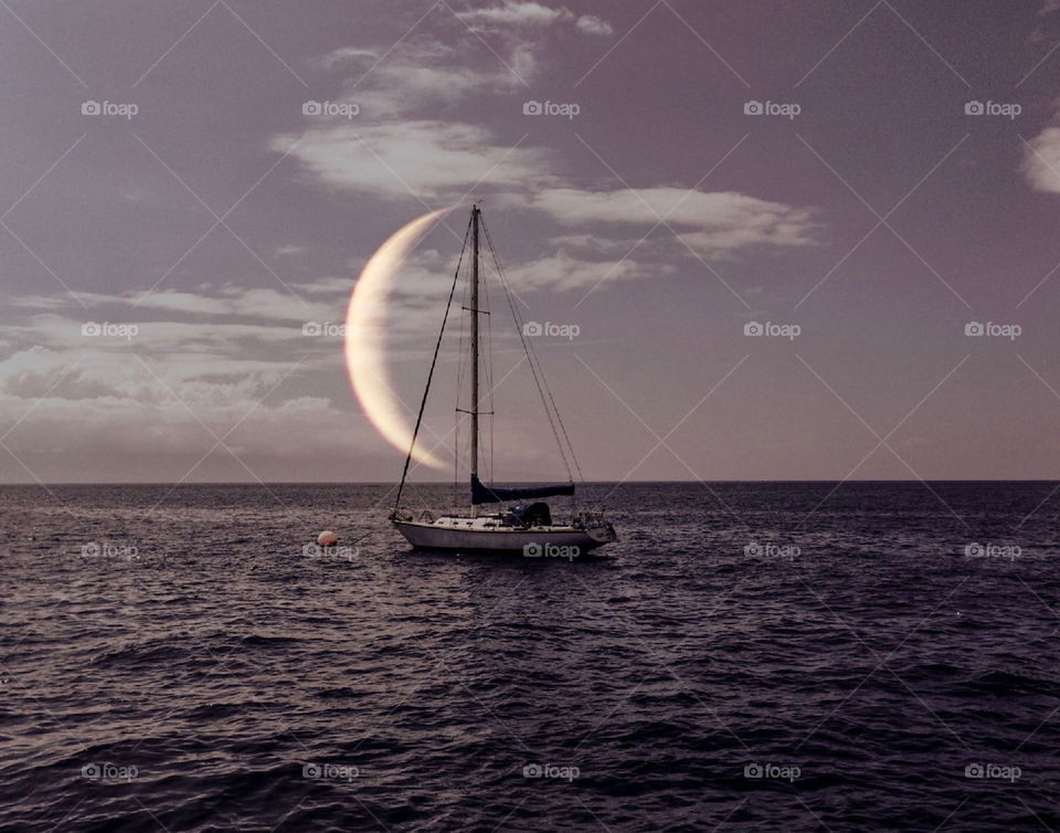 Sailboat on the horizon just as moon is coming up at dusk or night