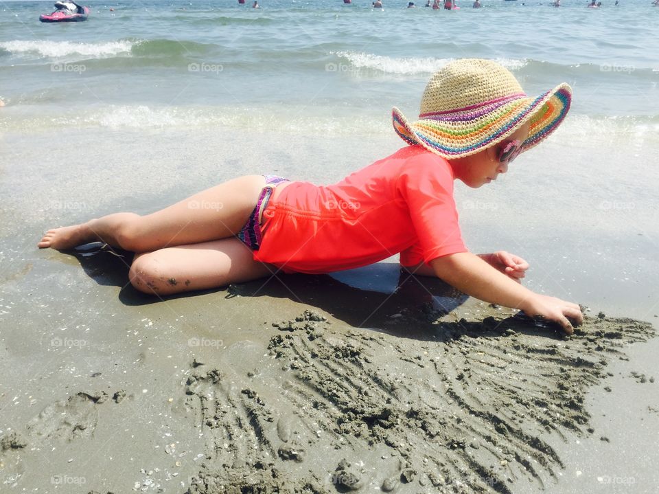 Little girl with fashionable summer hat playing in the sand on the beach