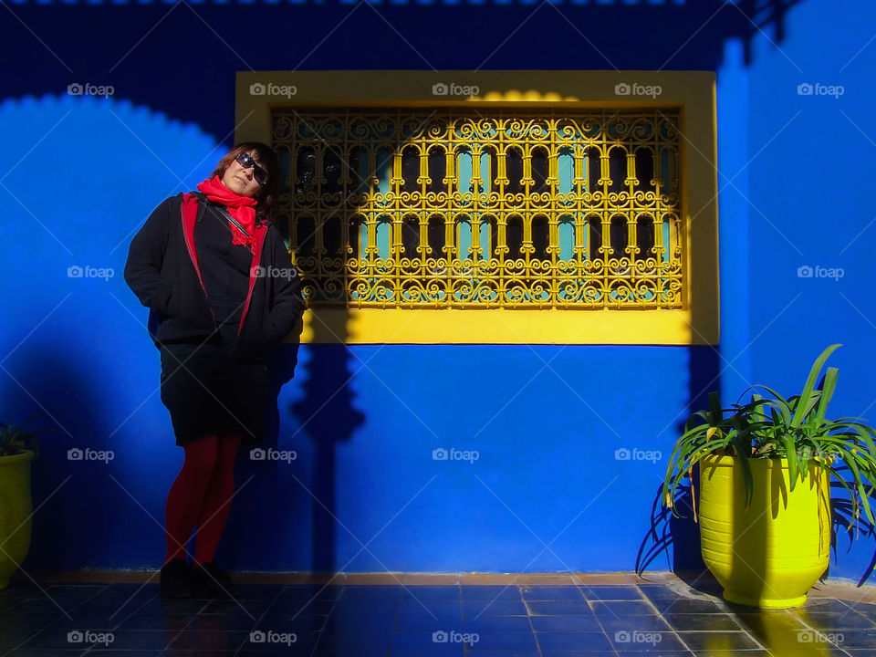 Girl with red scarf leaning on blue wall next to yellow framed window.