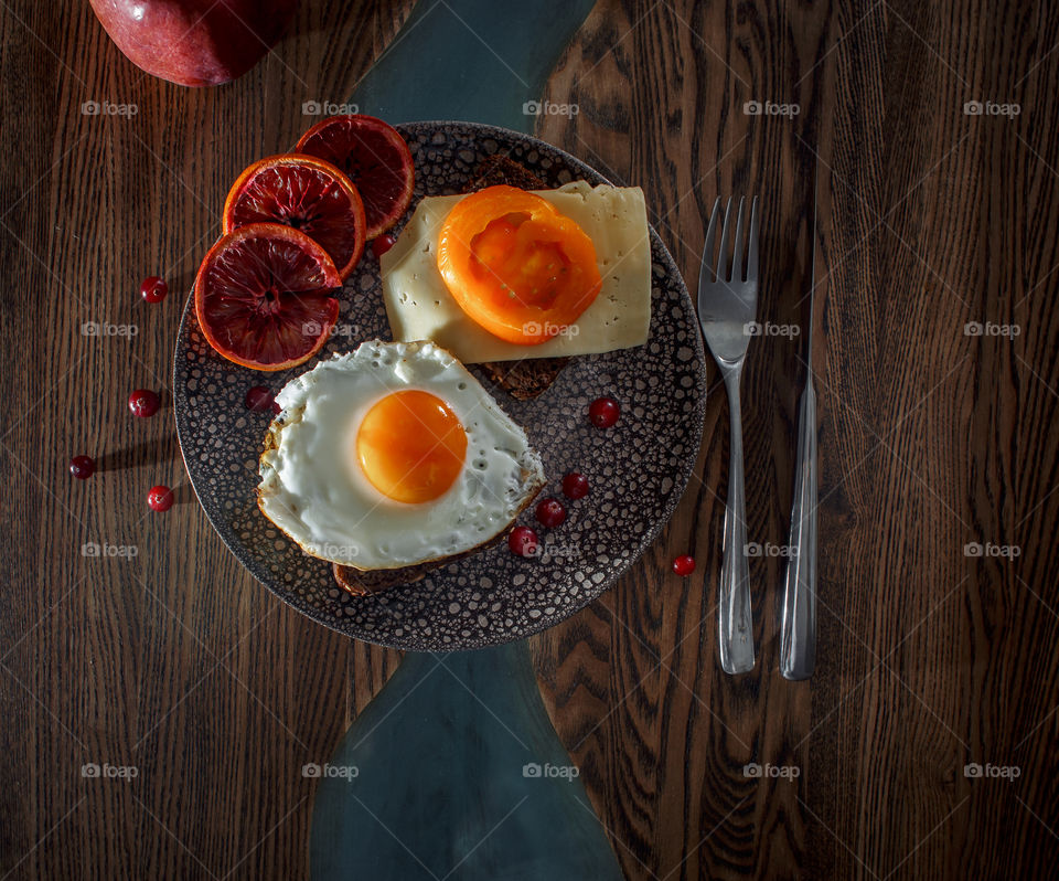 Grain bread with egg, tomato, cheese and bacon on ceramic plate with red orange to desert