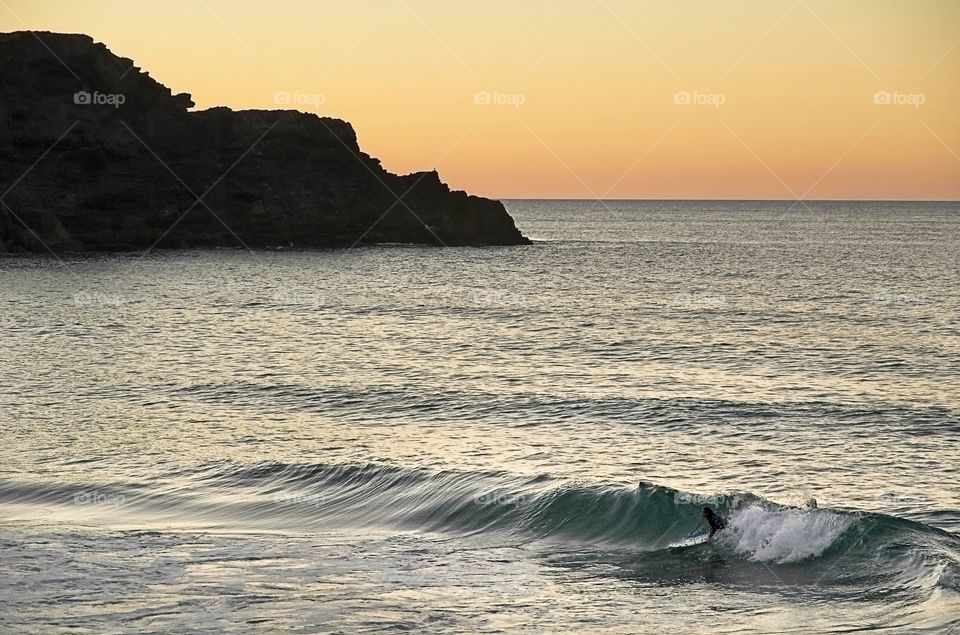 A lonely surfer catches the wave on a quiet beach at sunset