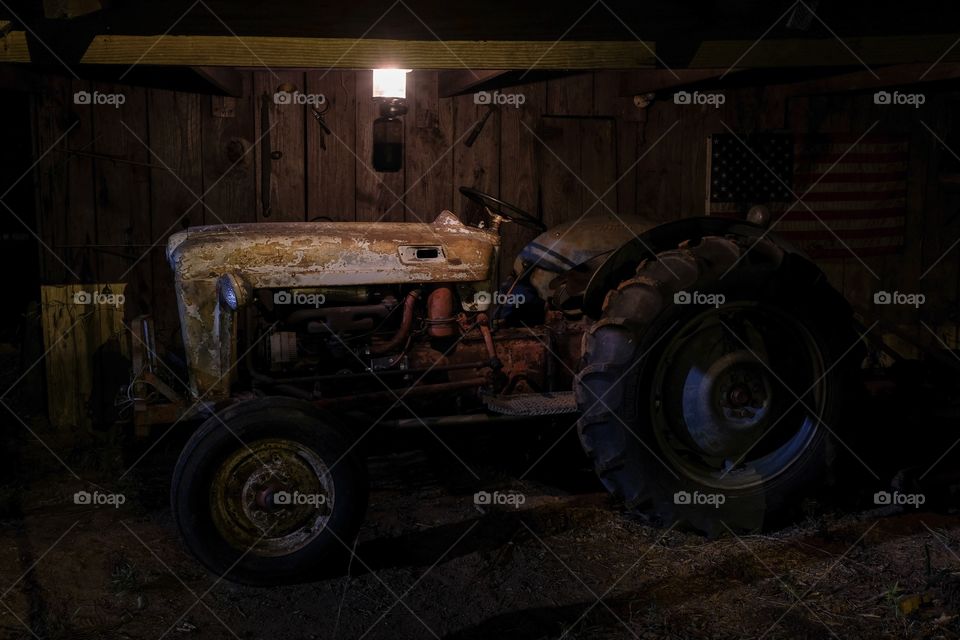 Profile view of a 1953 Ford Jubilee vintage tractor that is still operational under the dim light of a lantern in an old barn. 