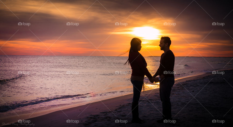 Silhouette of couple holding hand at beach during sunset
