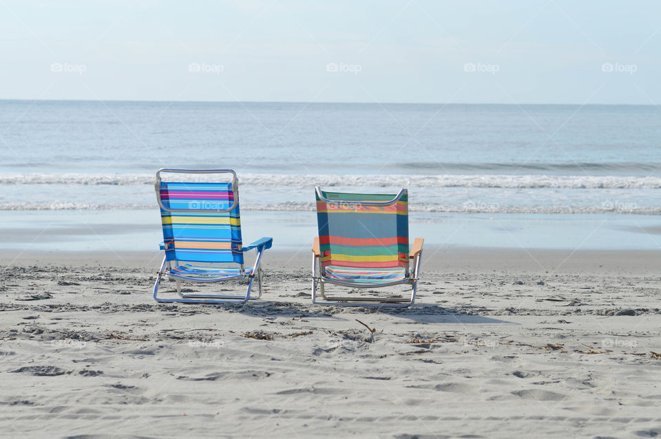 Two empty, colorful chairs on the beach overlooking the ocean