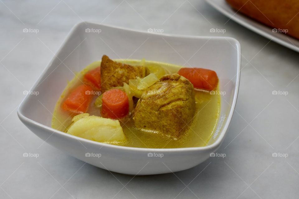 A bowl of chicken curry with carrots, potatoes, and onion in broth served with a baguette of French bread on the side