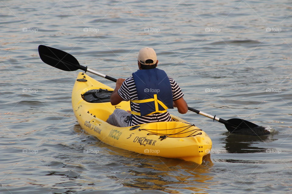 Man in blue life vest, striped shirt and beige baseball cap paddles bright yellow canoe on Hudson River on May Day 