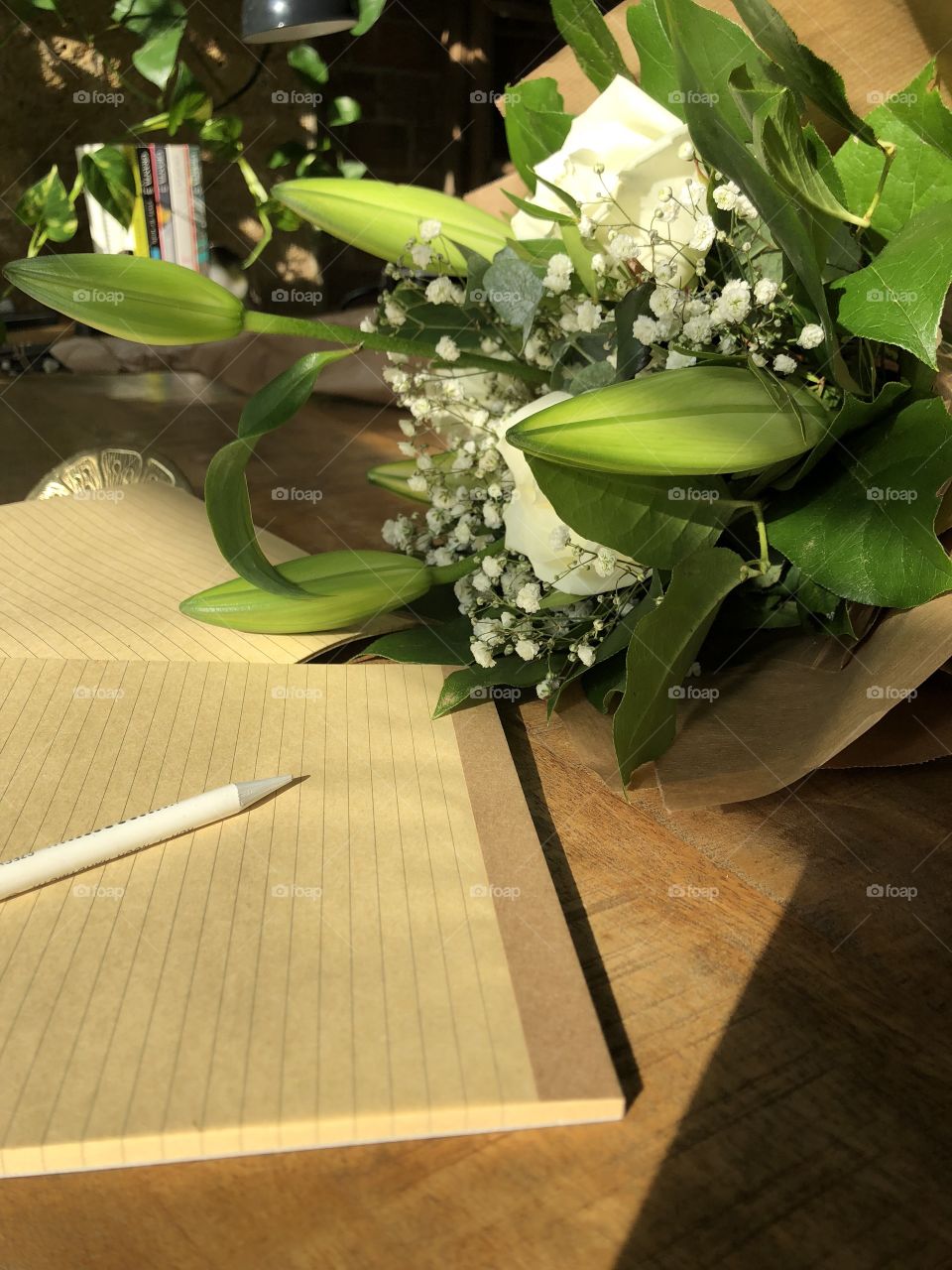 Wooden desk with rustic lined brown paper notebooks and cream and green floral bouquet in afternoon sunlight 