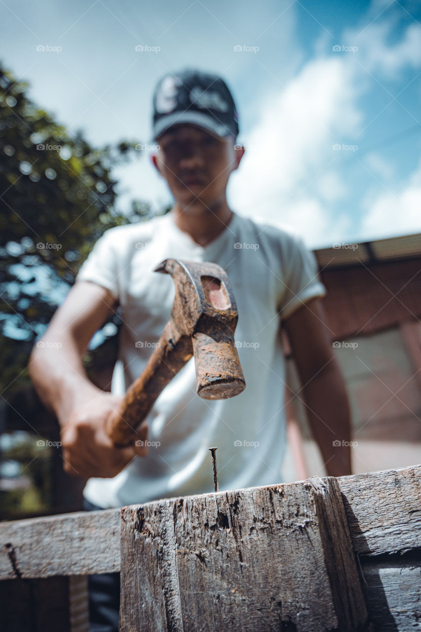 Boy nailing with a metal hammer to a little metal nail in the wood