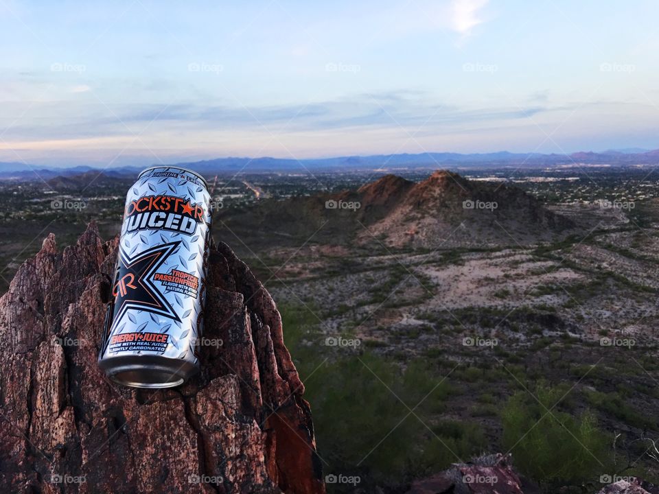 This photo features a Rockstar energy drink sitting at the top of a mountain overlooking a valley in Phoenix, AZ.