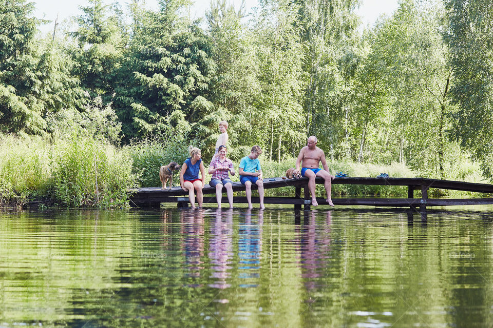 Family spending time together sitting on a bridge over a lake, among the trees, close to nature, during summer vacations. Candid people, real moments, authentic situations