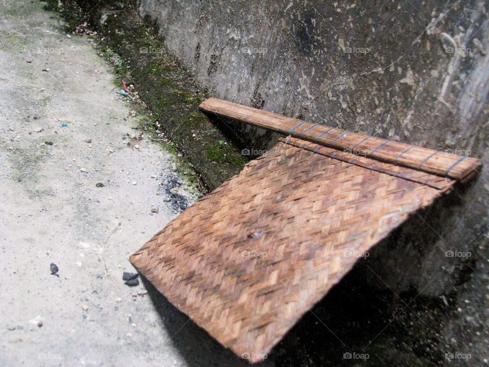 Close-up of a woven bamboo fan propped next to a dull old wall