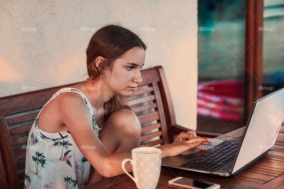 Woman working at home, using portable computer, sitting on patio on summer day. Candid people, real moments, authentic situations