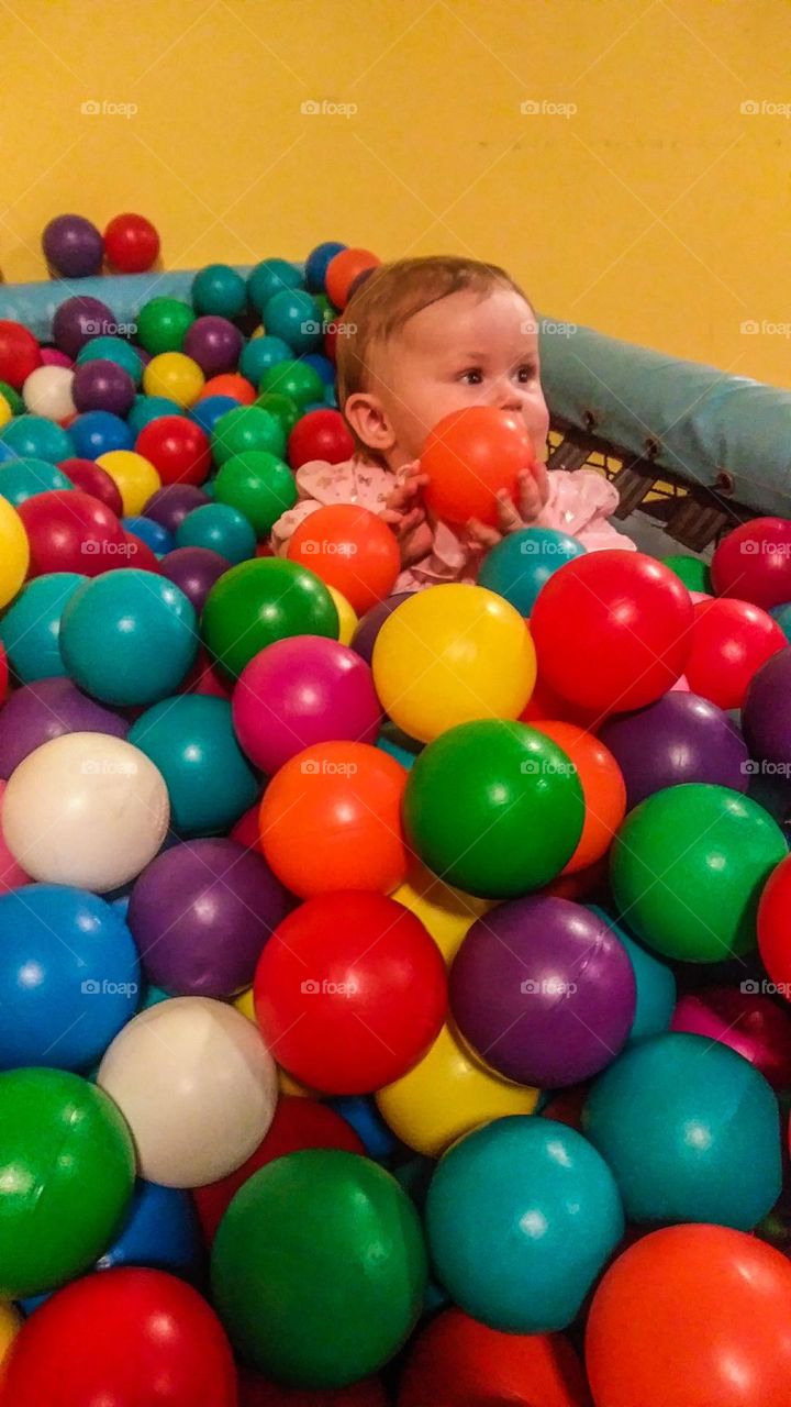 A baby holding a ball in a colorful ball pit 