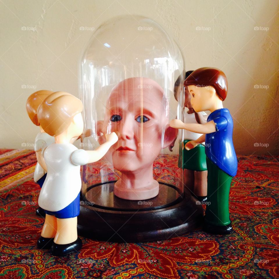 Under glass. Dolls trying to touch a bald dolls head under glass